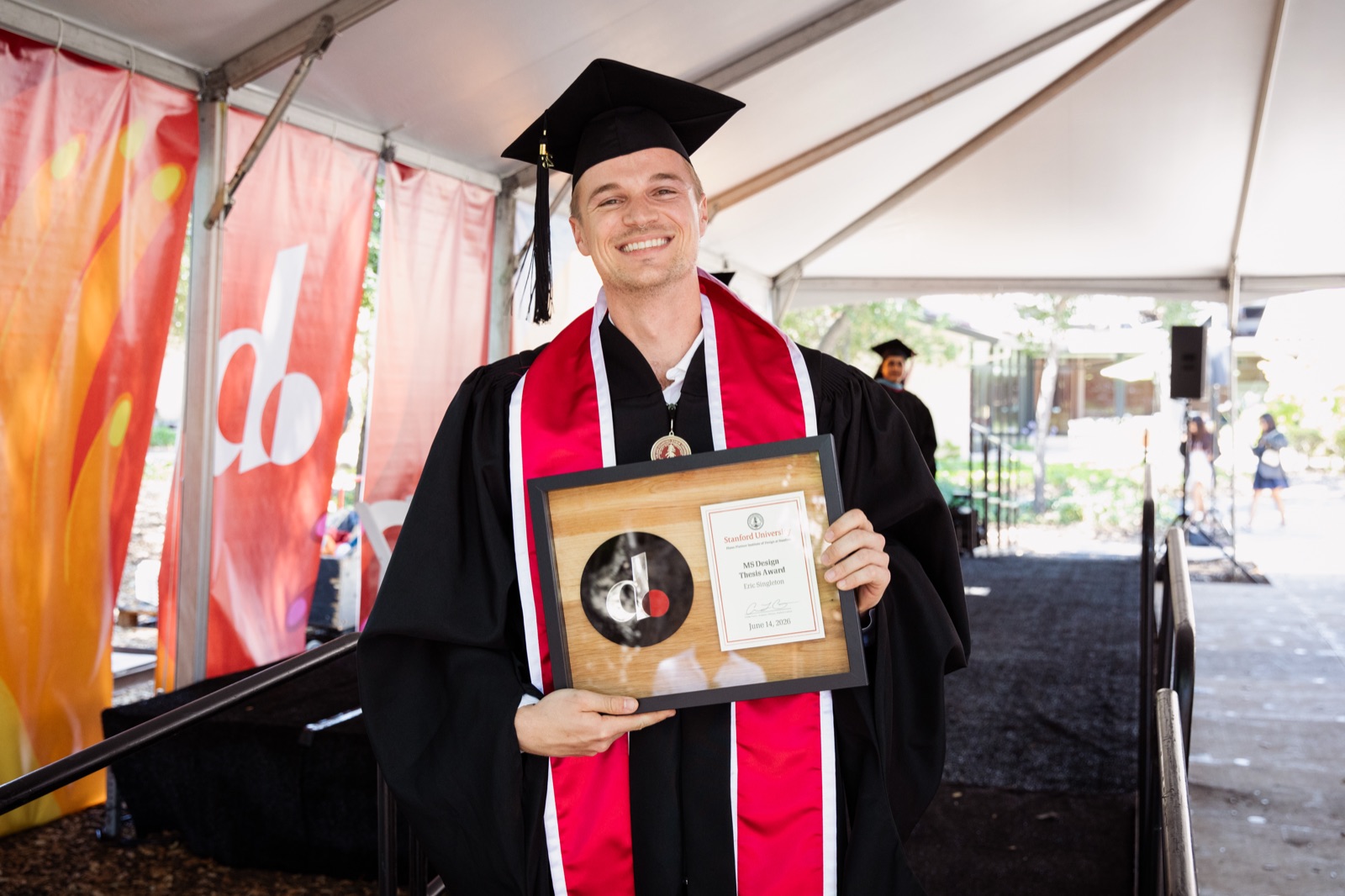 Eric in graduation regalia holding the MS Design Thesis Award plaque