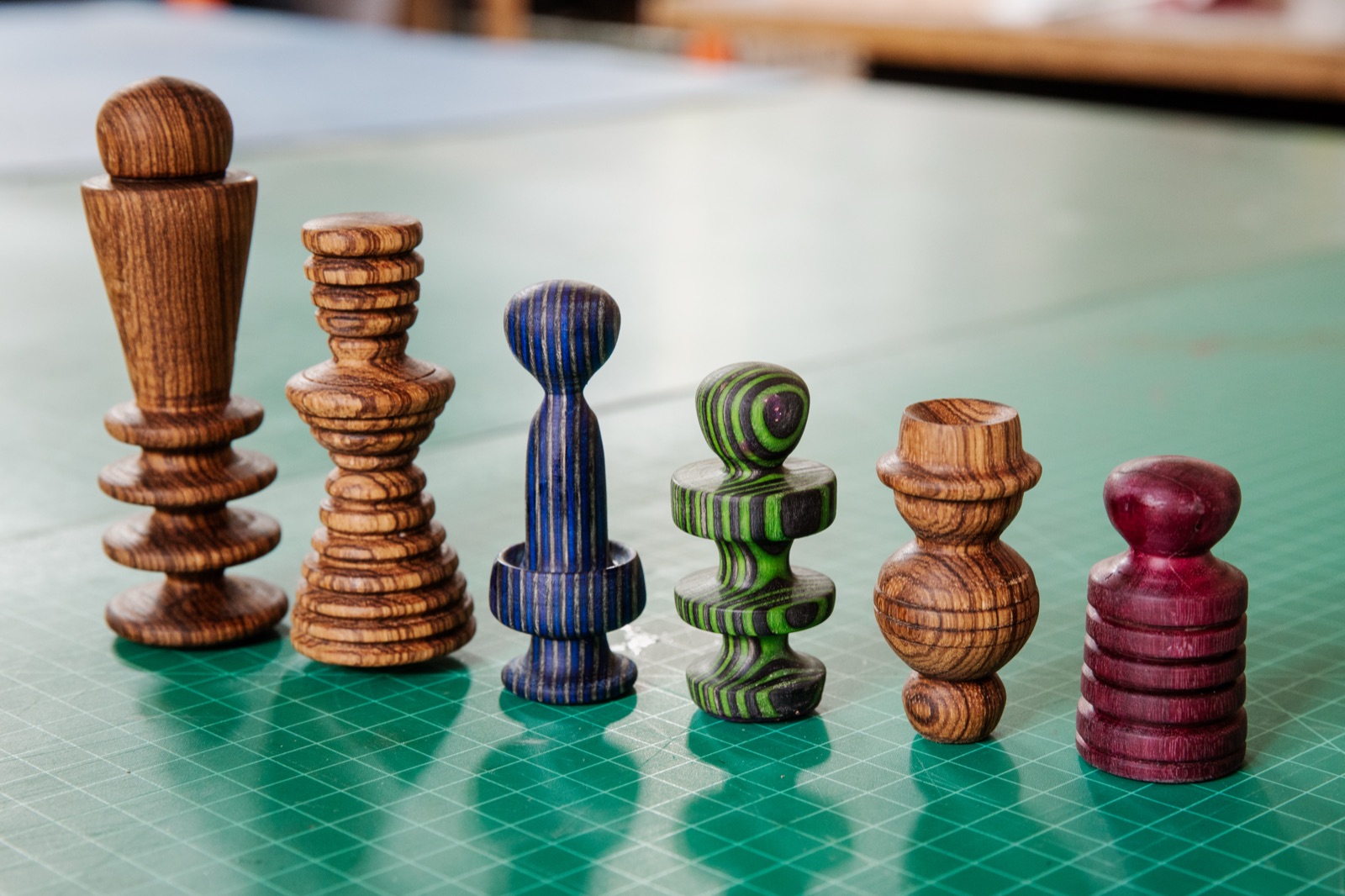 Six finished Edgers lined up on a green cutting mat, in turned hardwoods and dyed laminate