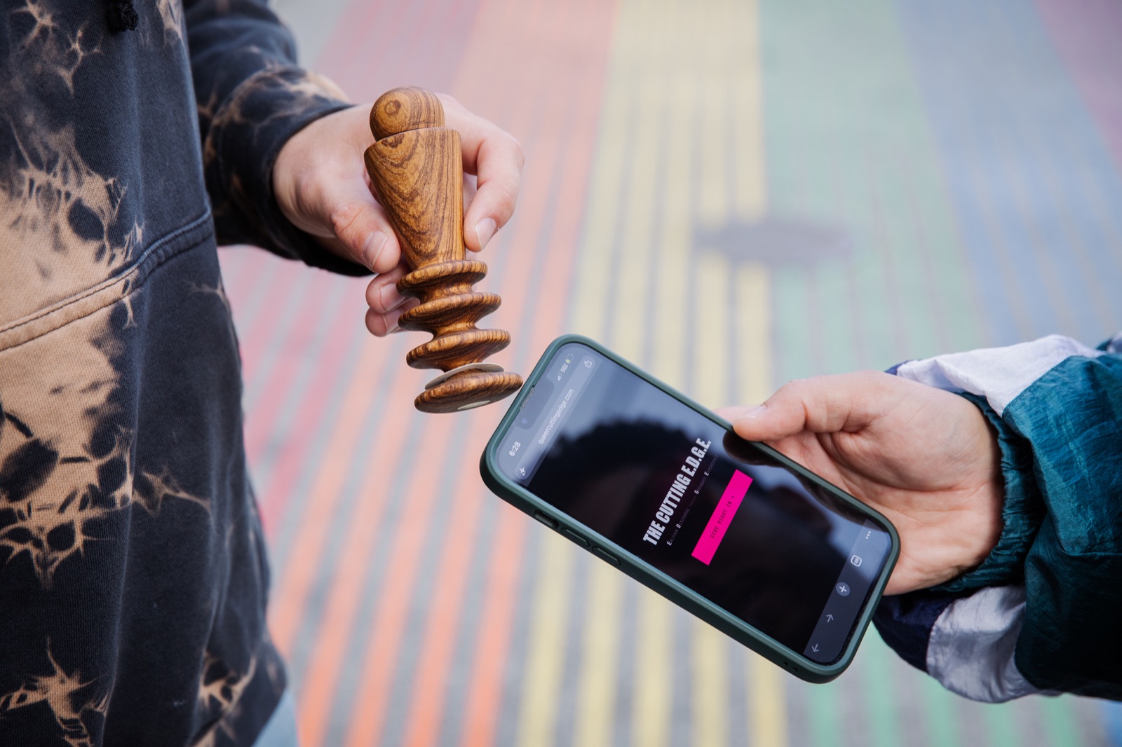 An Edger held to a phone that has opened The Cutting E.D.G.E. landing page, above a rainbow crosswalk
